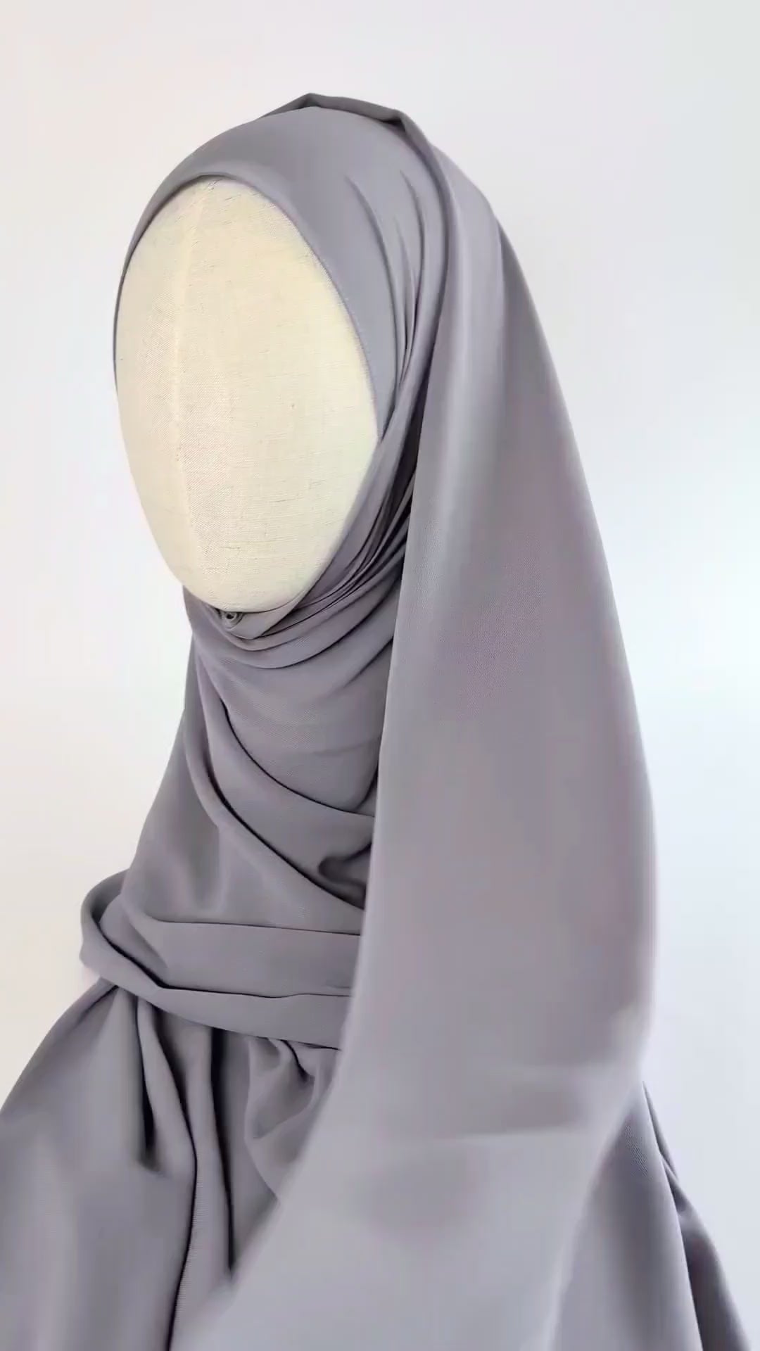 A light gray chiffon hijab draped over a cream-colored mannequin head in side face shot. the video focuses on how the hijab drapes gracefully and moves.