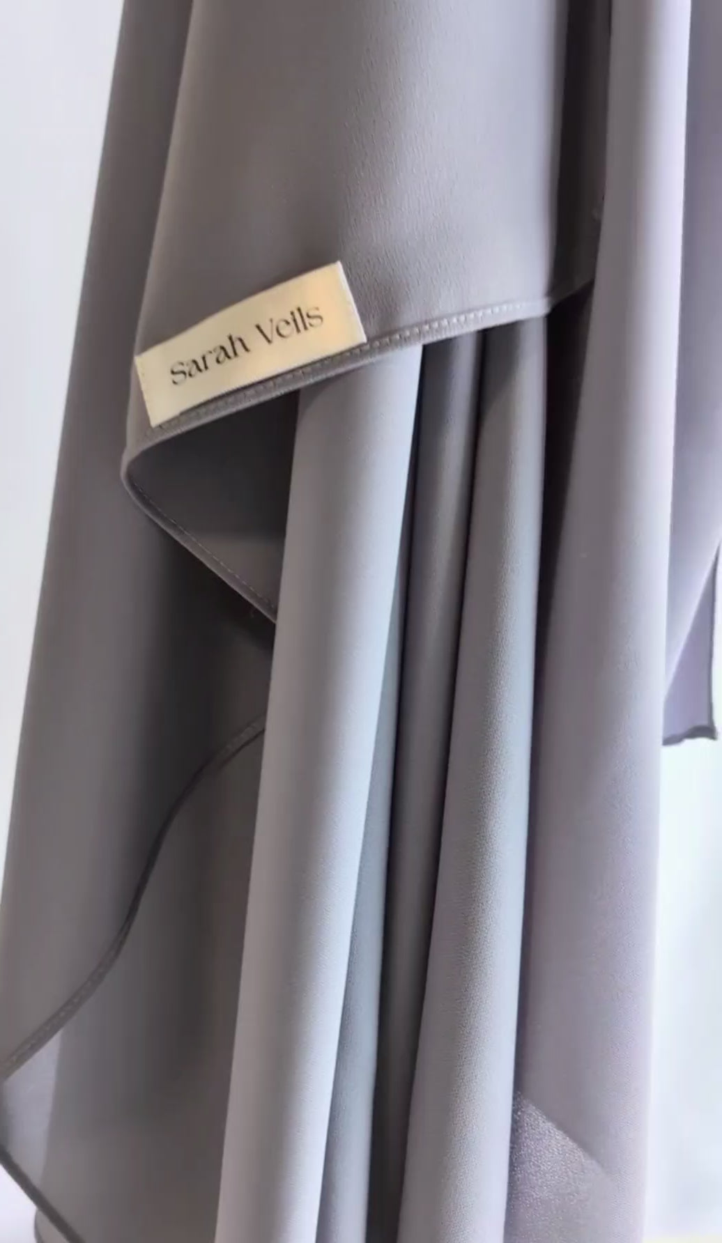 A short video of draped hanging chiffon hijab in light gray color gently moving side to side showing the drape and the airy chiffon hijab.