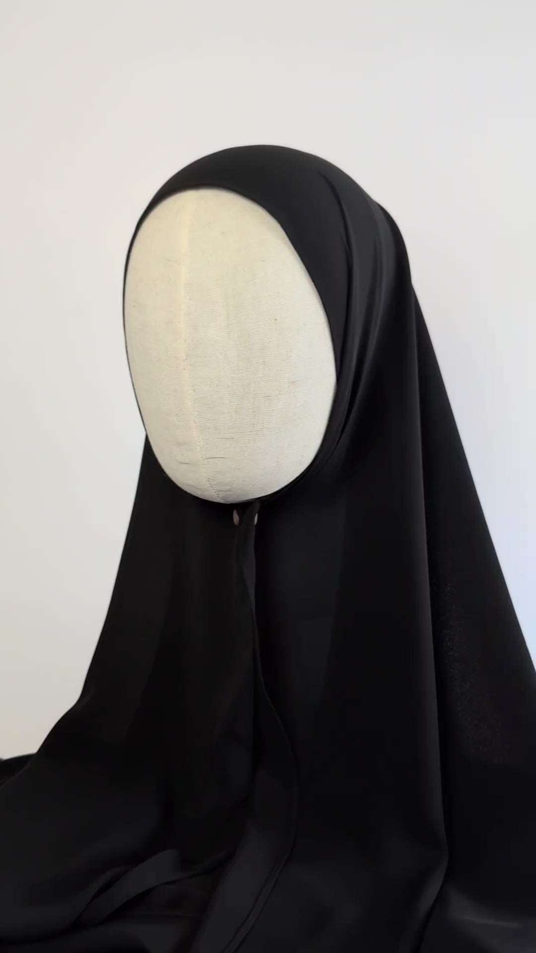 A close up video shot of a black hijab draped on a cream color mannequin head to show the soft texture and the drape of the chiffon hijab.