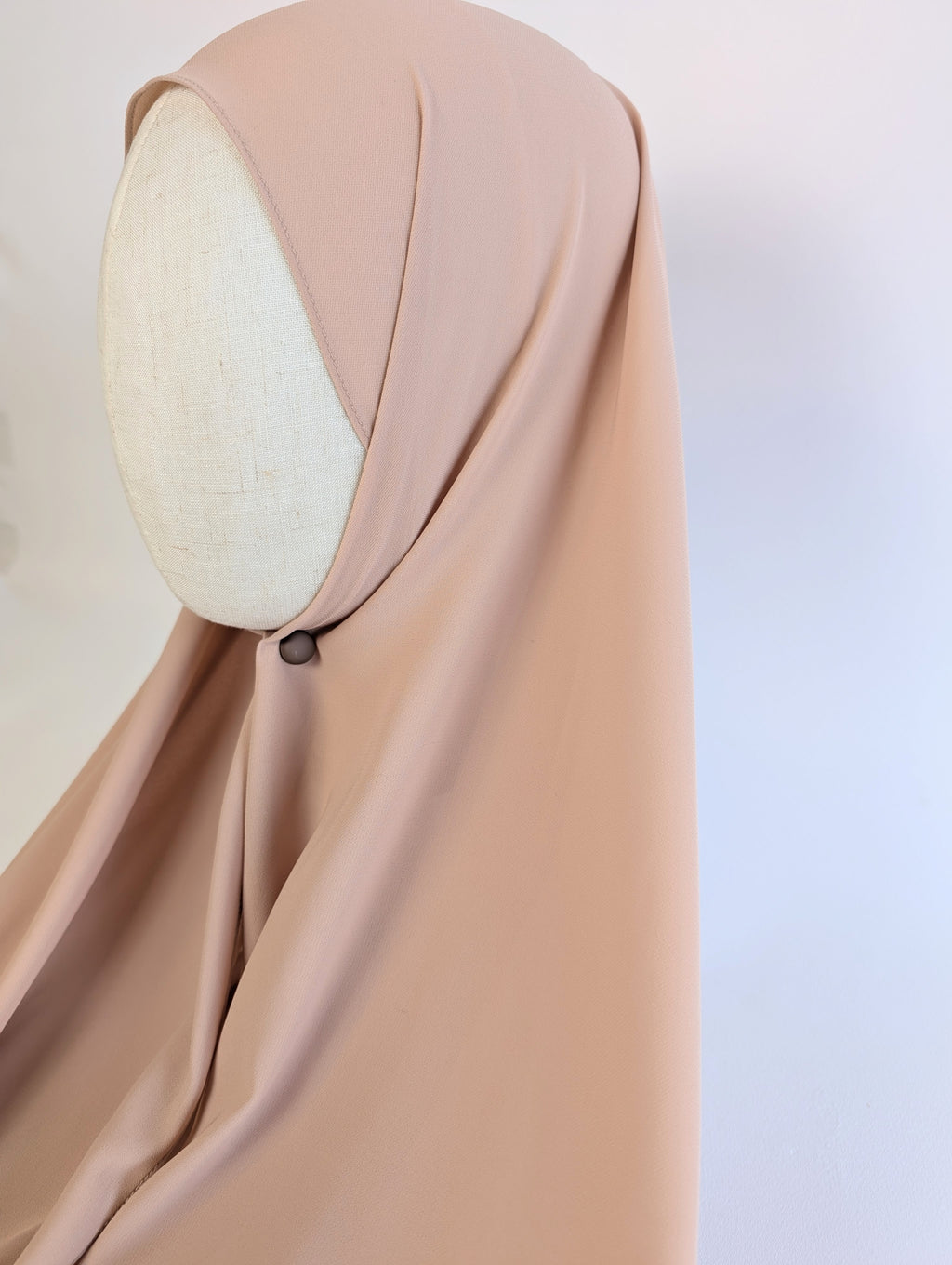 A draped Sarah Veils hijab in a soft beige or nude color, styled on mannequin head model in side face shot to show how it would fit and look on the customer