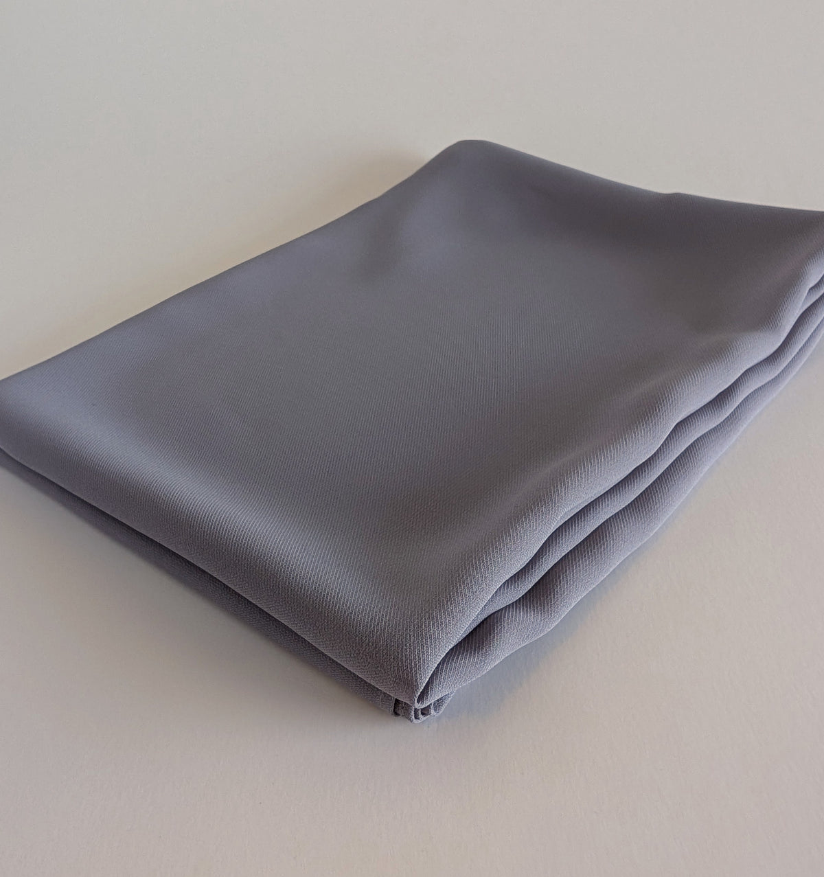 A folded piece of light gray chiffon hijab , displayed diagonally on a white background.
