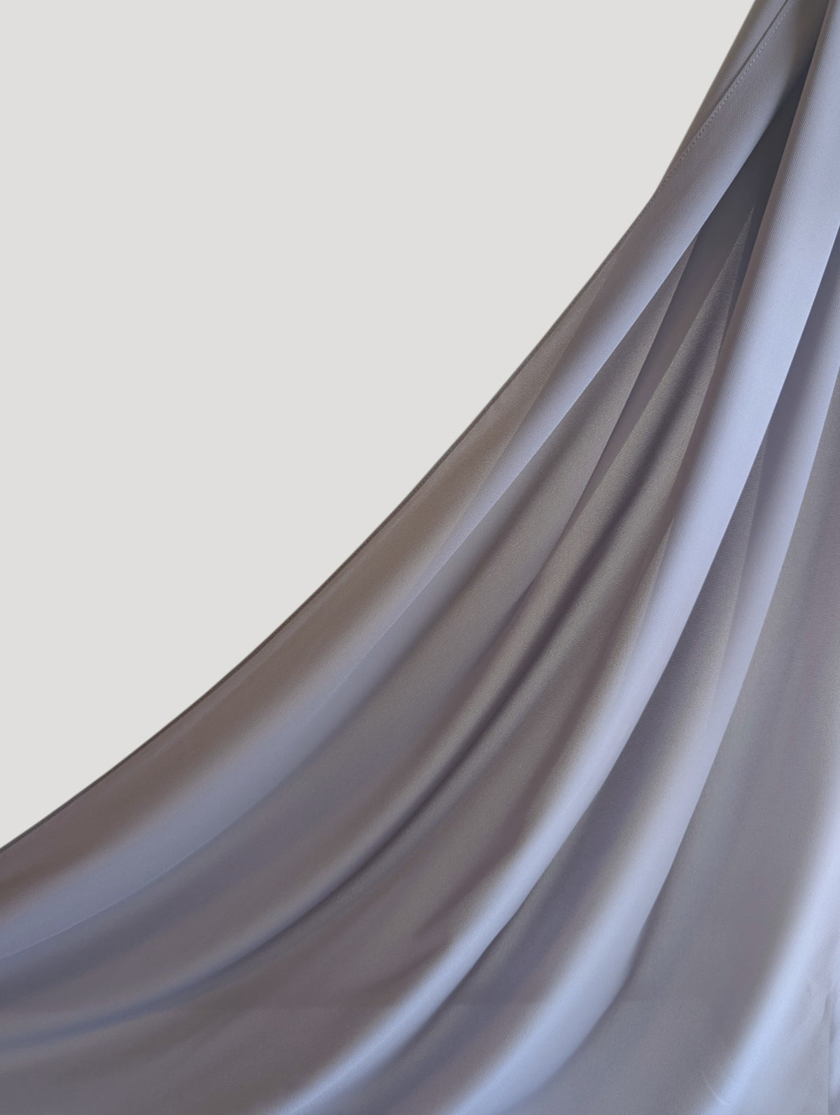 A close-up of draped premium chiffon hijab in light gray color, showing elegant folds and a smooth sheen against a white background.