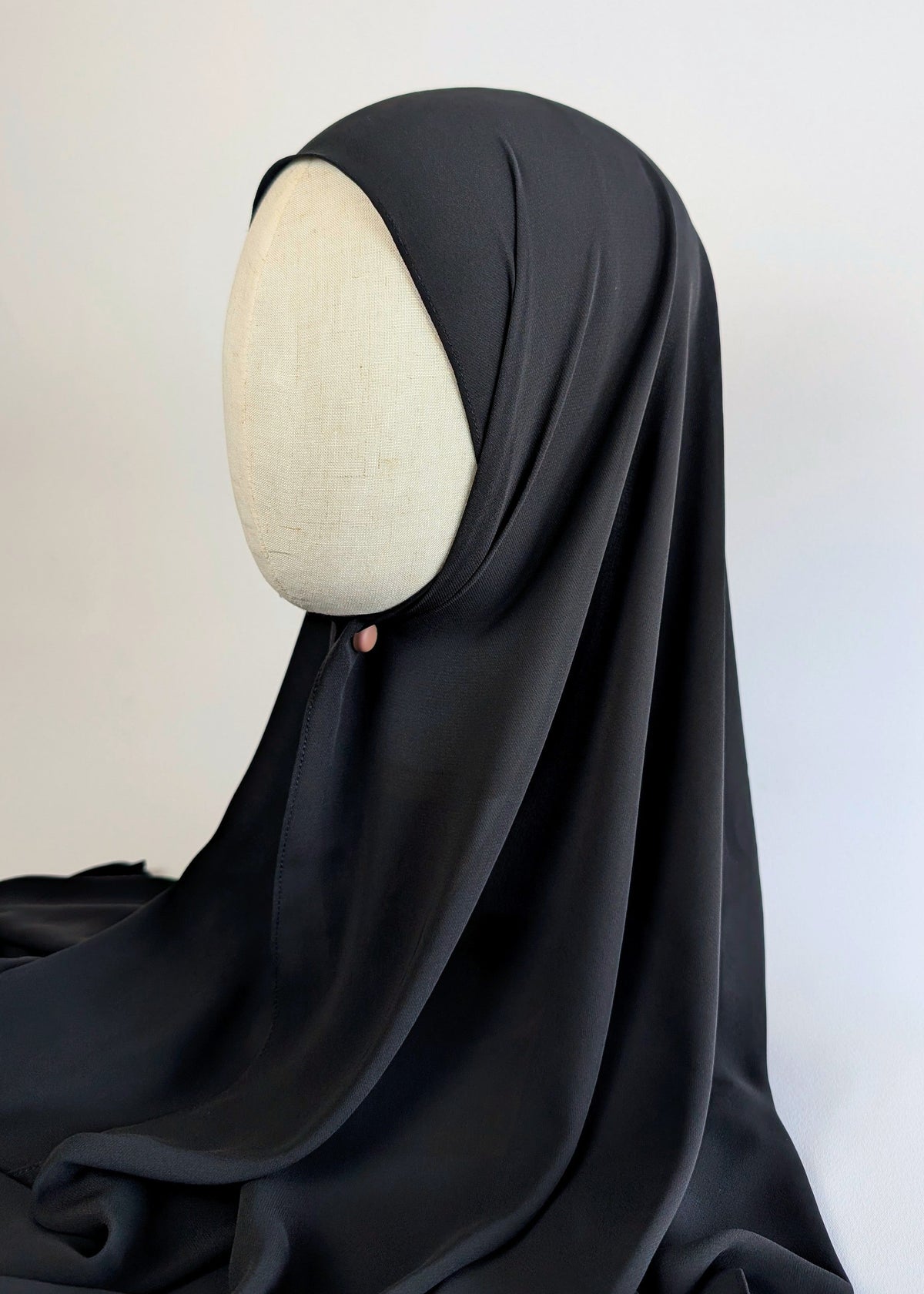 A black chiffon hijab draped over a cream-colored mannequin head in side face shot, photographed against a white background.