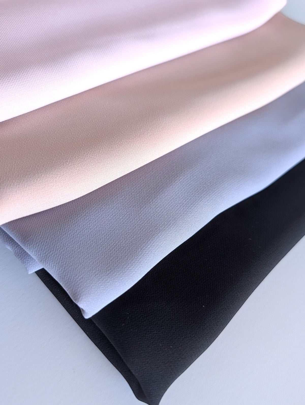 Four folded chiffon hijabs in light pink, pale beige, light gray, and black, arranged diagonally on a white background featuring a hijab bundle offer.